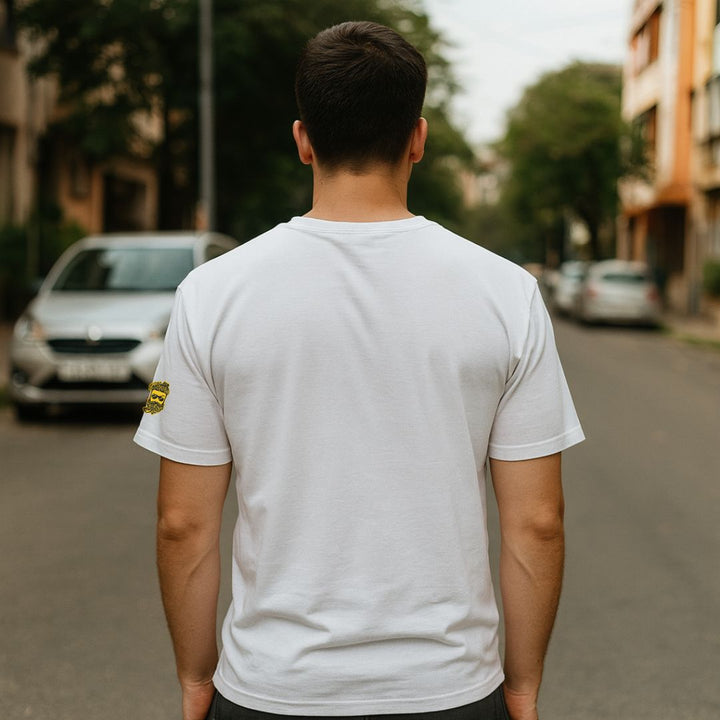 Man wearing a white t-shirt with a small yellow logo on a street.