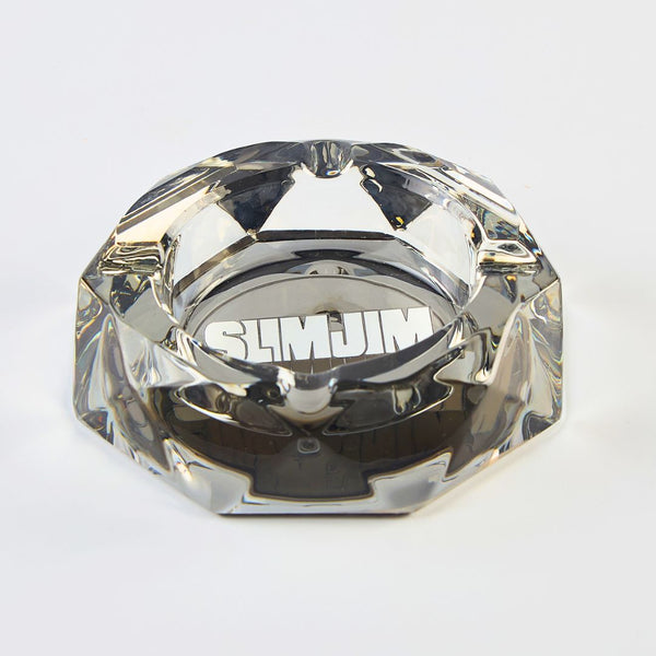 Clear glass ashtray with 'Slim Jim' branding on a light gray background