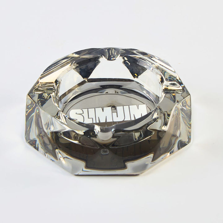 Clear glass ashtray with 'Slim Jim' branding on a light gray background
