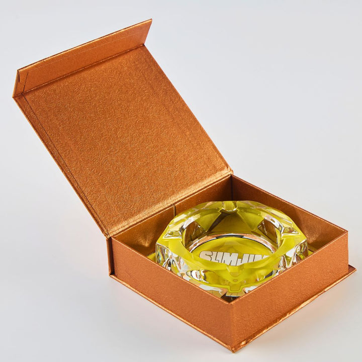 Clear glass ashtray with Slimjim branding inside an open brown box on a white background
