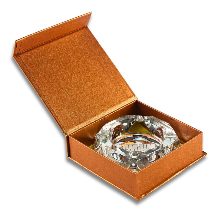 Clear glass ashtray in an open brown box on a white background