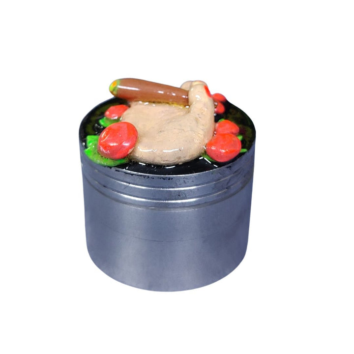 Metallic crusher with a decorative item on top featuring a turkey, hot dog, and flowers.
