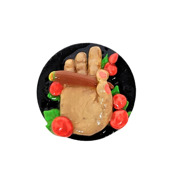 Decorative item with a hand holding a hot dog surrounded by red apples and green leaves on a black background.