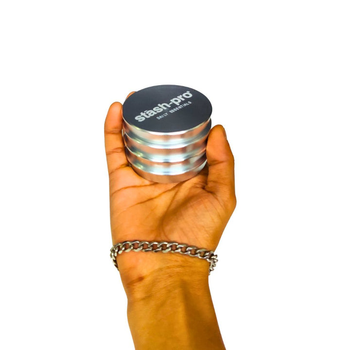 Hand holding a silver and black 'stash-pro' grinder against a white background